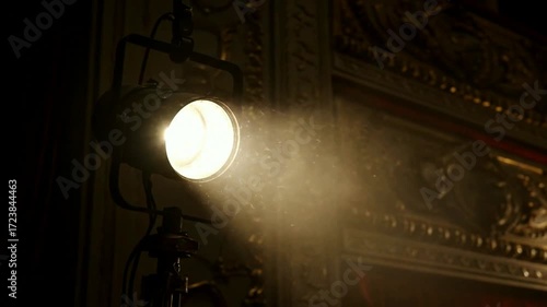A vintage stage light in an ornate theater turns on its bright beam cutting through atmospheric smoke and dust particles