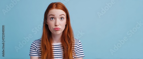 The redheaded woman making a puzzled pout against a blue studio background