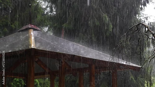 Heavy rain falls on the roof of a gazebo in a garden in slow motion