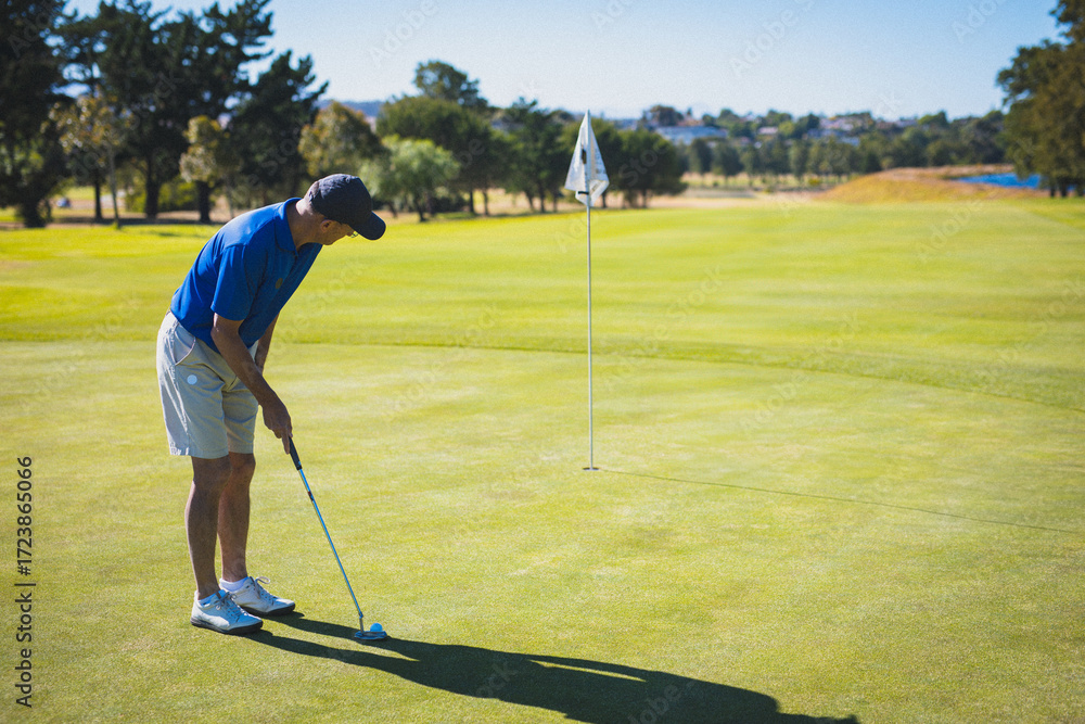 Obraz premium Senior golfer lining up putt on putting green with putter, golf ball near flagstick, copy space