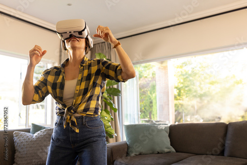 Woman using virtual reality headset interacting with environment in living room near sectional sofa
