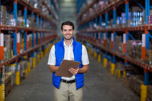 Warehouse supervisor inspecting boxes on metal racks with clipboard and pen near yellow bollards