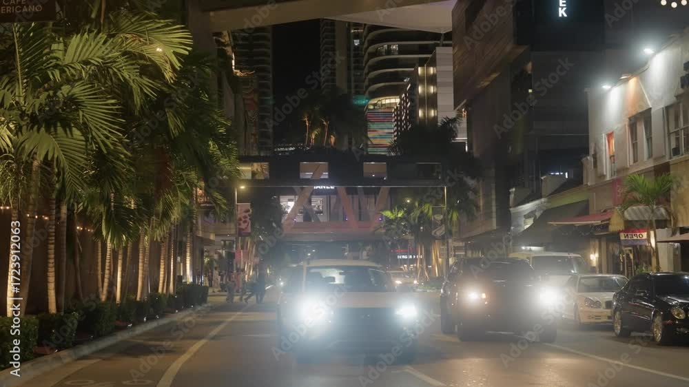 Night view of pedestrians crossing streets and cars driving in Miami Brickell. Urban cityscape with traffic, street lights, and downtown skyline at night