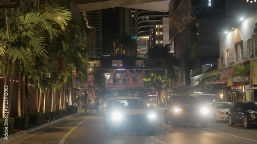 Night view of pedestrians crossing streets and cars driving in Miami Brickell. Urban cityscape with traffic, street lights, and downtown skyline at night