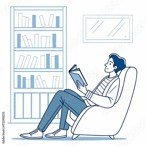 Young man sitting comfortably in a chair reading a book next to a bookshelf
