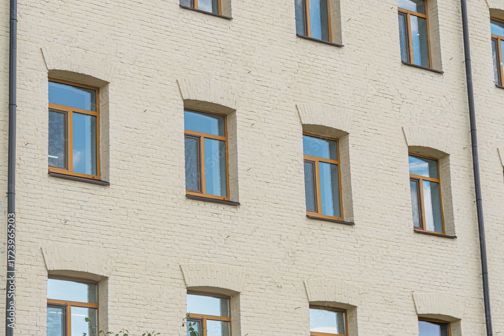 Obraz premium An older, light-brick building with evenly spaced windows framed in wood, displayed under natural daylight a