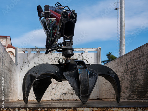 Industrial hydraulic grapple claw attachment inside truck container, showing black jaws, hoses, and rotator. Heavy-duty scrap metal handler used in recycling, salvage, demolition, and construction.