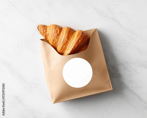 Golden flaky croissant in a brown kraft paper bag with blank round label - ideal for bakery packaging mockups or product presentations