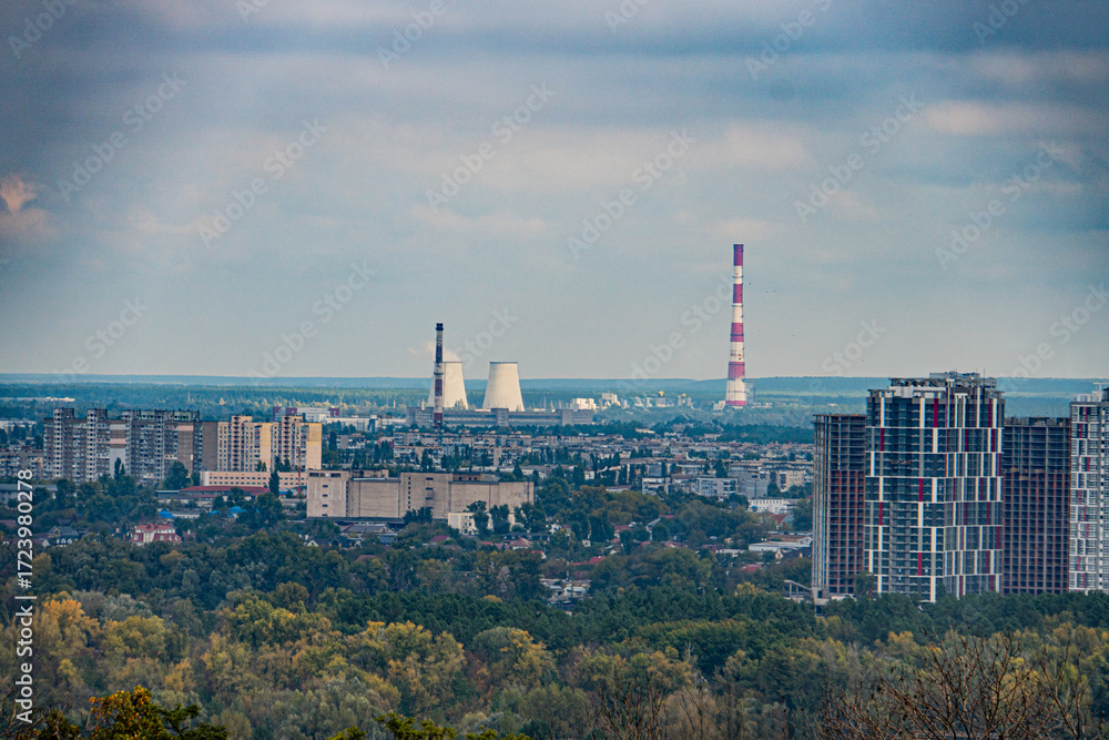 Obraz premium Aerial view of Kiev cityscape with a mix of green and yellow trees, diverse architecture including a prominent white striped water tower, power lines crisscrossing above buildings, overcast sky
