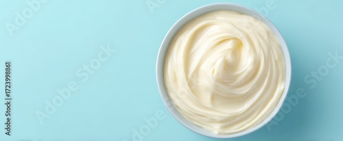 The bowl of creamy mayonnaise on pastel blue background with smooth swirl