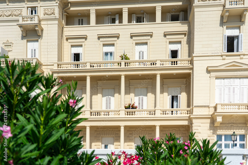 Fototapeta premium Elegant neoclassical building facade with balconies, shutters, and blooming flowers