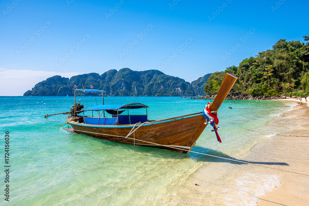 Fototapeta premium Traditional Thai longtail boat resting on Long Beach in Phi Phi Don, showcasing stunning views of crystal clear waters and lush green hills in Krabi, Thailand