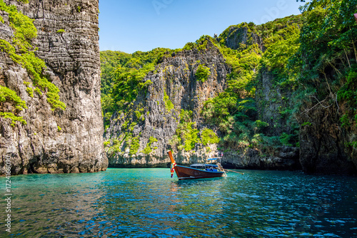Longtail boat floating on calm turquoise water surrounded by towering limestone cliffs covered in lush tropical vegetation, capturing the essence of a serene island vacation in Southeast Asia