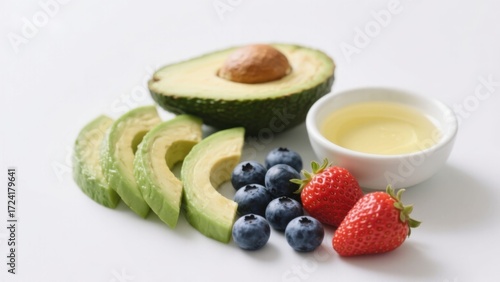 Sliced avocado, blueberries, strawberries, and a small bowl of oil arranged on a white surface