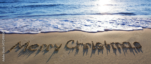 Merry Christmas handwritten on the sea sand.