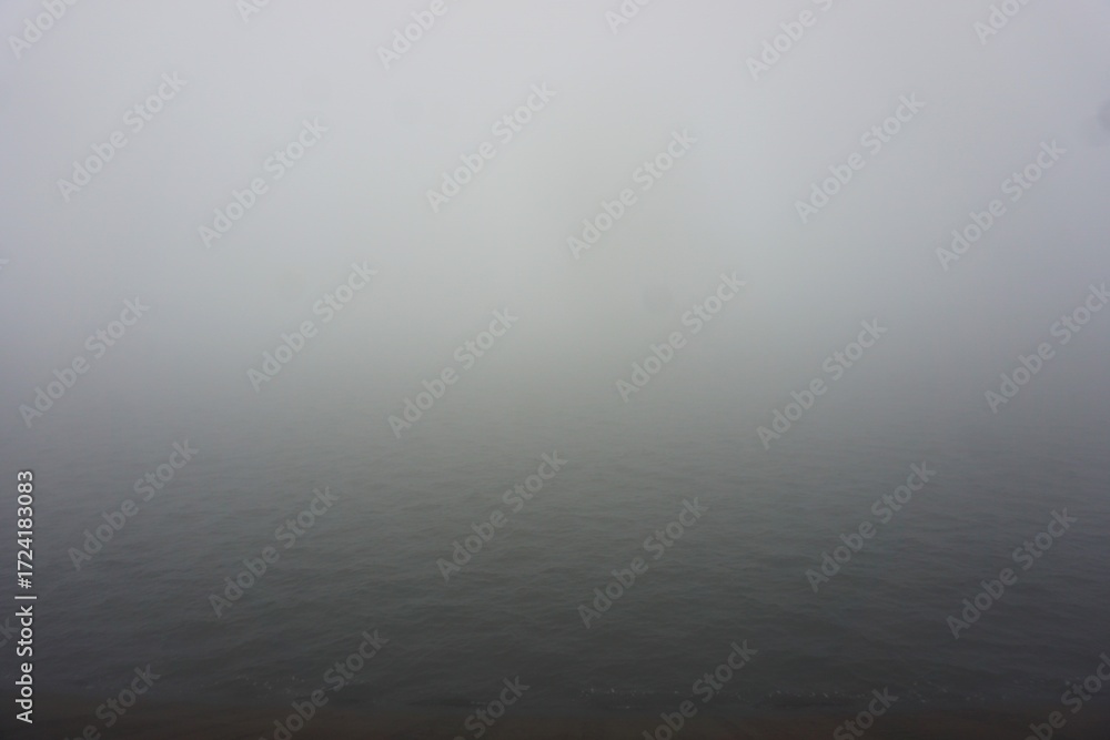 Fototapeta premium Gęsta mgła unosząca się nad jeziorem, tworząca mroczny i tajemniczy klimat. Widoczna jedynie spokojna tafla wody i mgła spowijająca cały obszar. Nastrojowy pejzaż natury o ograniczonej widoczności.
