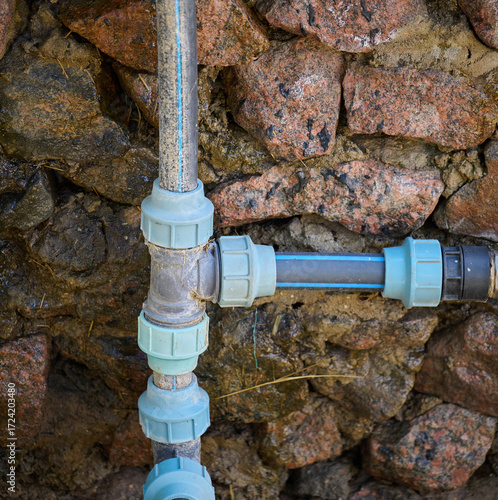 Plastic water pipes with fittings installed on a wall made of large stones