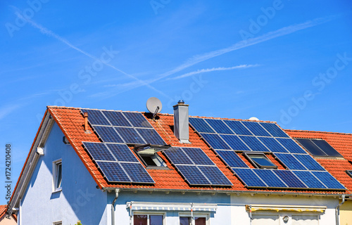 Wohnhäuser mit Solaranlagen zur Erzeugung von Strom und Warmwasser auf roten Hausdächern vor blauem Himmel