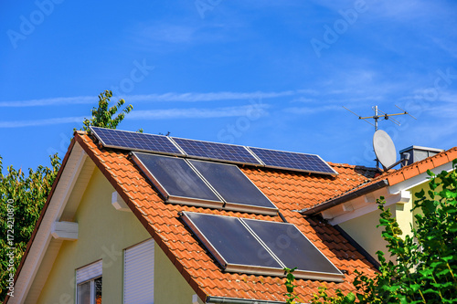 Solaranlagen zur Erzeugung von grünem Strom und Warmwasser auf rotem Hausdach vor blauem Himmel