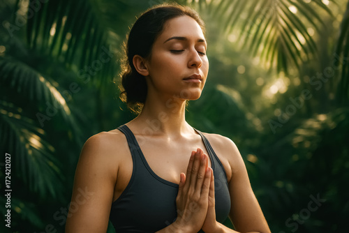 Calm woman practicing meditation with hands in prayer pose amid lush tropical greenery at sunrise. Wellness and peace. generative AI