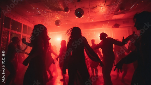 Silhouettes of people dancing in a dimly lit room with red lighting and disco balls.