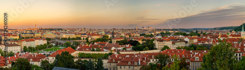A breathtaking panoramic view of Prague showcasing the historic cityscape with red rooftops, the majestic Prague Castle, and the winding Vltava River under a golden sunset sky.