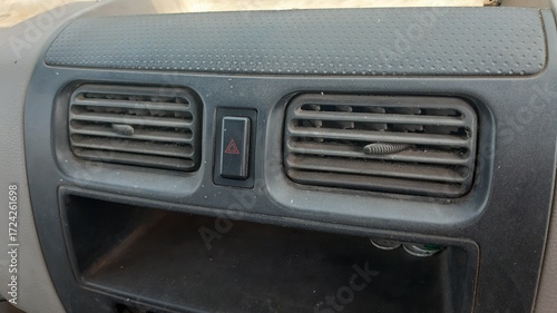 Second dashboard vent with hazard button covered by fine dust on textured plastic panel.