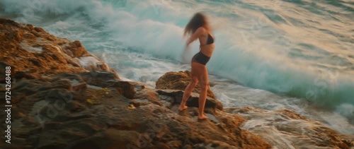 Blurry view of woman dancing beside powerful waves crashing on volcanic rocks