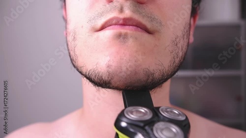 Close-up of a man shaving his beard with a black razor, a topic of hygiene and personal image