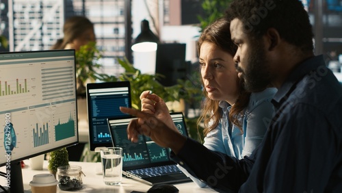 Team leader showing employee mistakes to fix in business documents on PC. African american man and manager analyzing company information records in office using computer, camera A