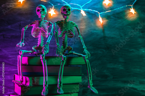 Magic books set, Garland with stars and decorative skeleton with gradient light. Skeleton figurine on a stack of books with a shimmering garland in purple and blue mysterious light.Scary Autumn Books 