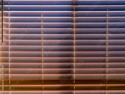 Sun shining through faux wood Venetian blinds hanging on a window