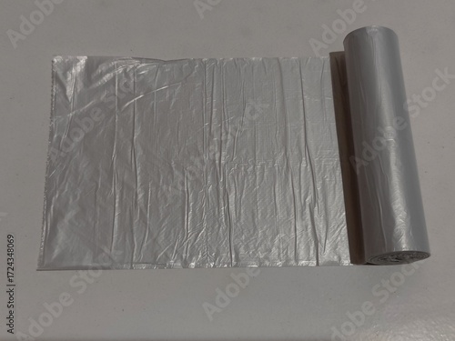 A silver garbage bag roll partially unrolled on a white background. Suitable for cleaning, waste management, and household concepts