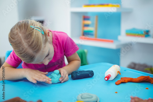 Modeling clay pieces resting on bright blue plastic table with glue bottle and colorful shelving