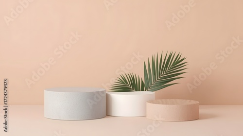 Minimalist composition with three modern cylindrical podiums in gray, white, and terracotta colors, decorated with green palm leaves on pastel background for product display