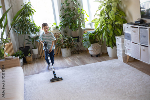 A white-skinned neat child does his household chores. He vacuums a carpet in the living room