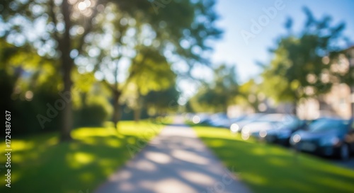 Fototapeta Naklejka Na Ścianę i Meble -  Sunlit park pathway with blurred trees and parked cars bokeh image