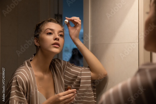 Wallpaper Mural Beautiful young woman taking care of her face at home, skincare procedures, selective focus. Portrait of a woman applying a serum and doing face massage for her face in her bathroom. Real photo. Torontodigital.ca