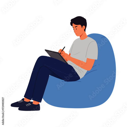 A young man sits in a blue beanbag chair, drawing or writing on a digital tablet with a stylus.