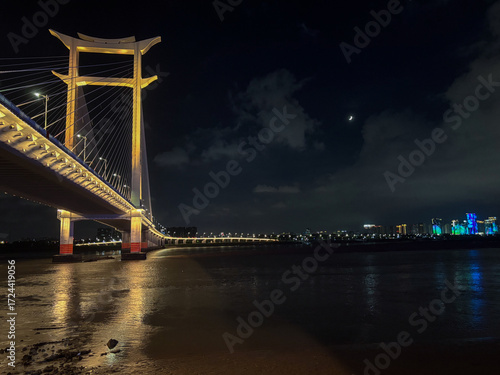A imponência noturna da ponte iluminada em Guangzhou, refletindo sobre o rio e conectando a modernidade da cidade com sua elegância arquitetônica.