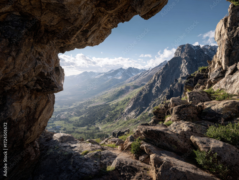 Fototapeta premium Mountain view through rock formation showcasing rugged terrain, lush greenery, and distant peaks under a clear blue sky with clouds creating a serene outdoor atmosphere.