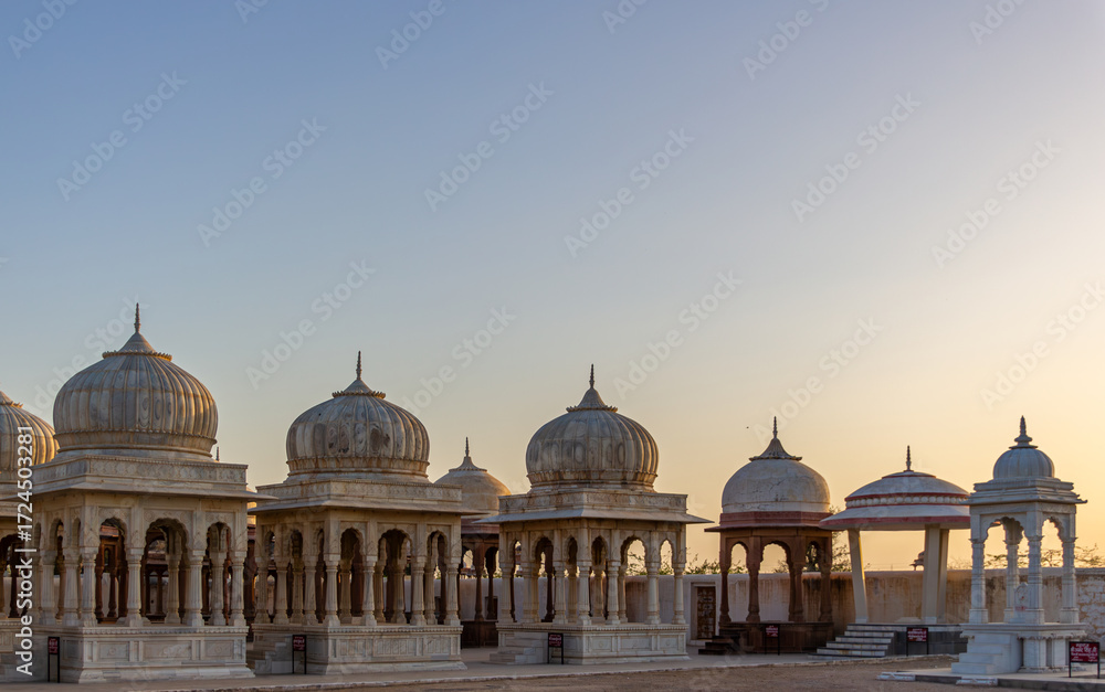 Obraz premium Ancient Stone Cenotaphs with Ornate Domes and Pillars Under a Clear, Golden Sunset Sky