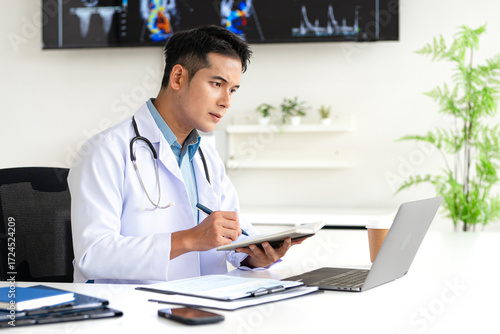 Serious mature professional  doctor using laptop computer in hospital office watching medical webinar training, writing in healthcare report, consulting patient online at telemedicine meeting.