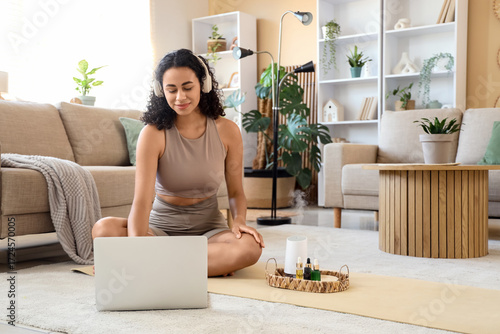Remote work and wellness, woman using laptop on yoga mat at home with essenti...