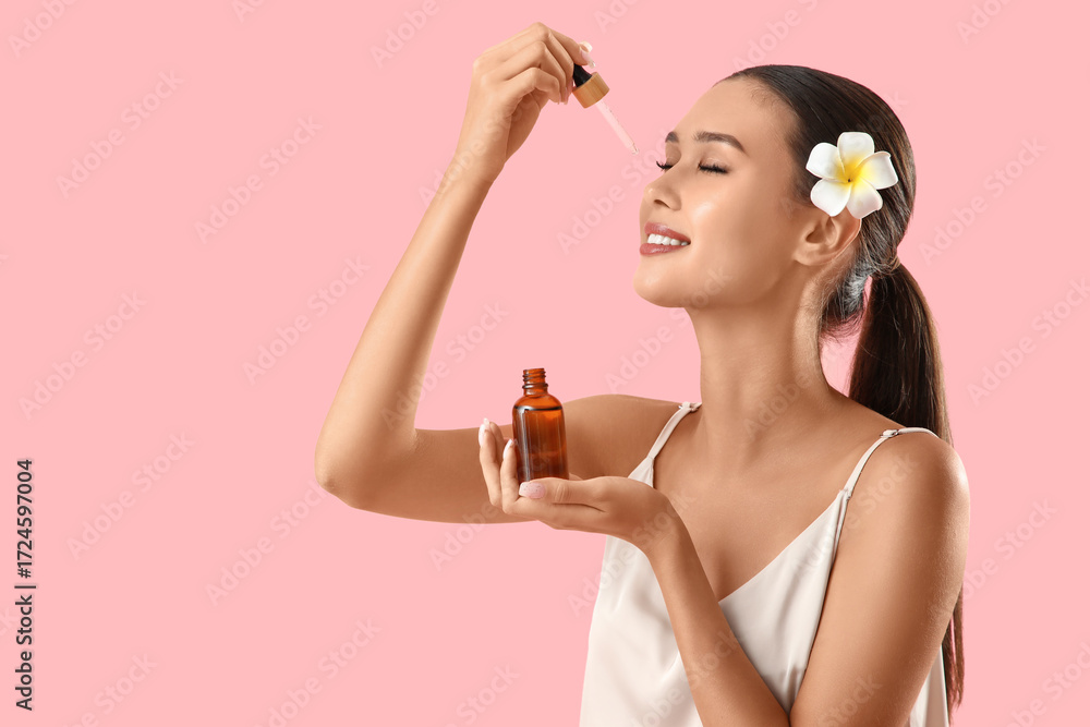 Fototapeta premium Young woman applying serum with vitamin E on pink background