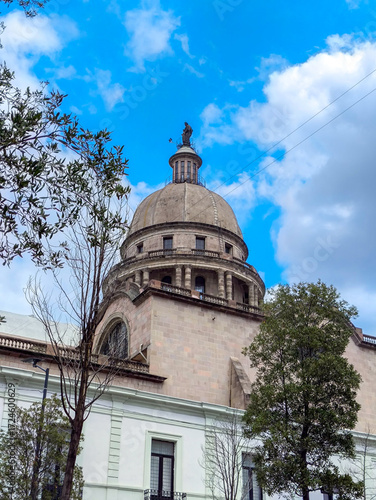 Cathedral old building dome with statue and trees under a blue sky