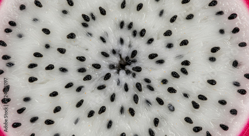 A strikingly detailed macro shot showcases the intricate texture and composition of dragon fruit, revealing its vibrant white flesh speckled with numerous small, black seeds arranged in a spiral