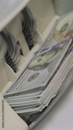 Stacks of US dollars being processed and counted in an automatic money counting machine.