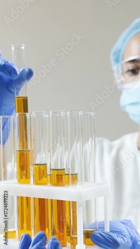 Scientist in lab coat and gloves examines golden oil in test tubes, pouring and analyzing samples.