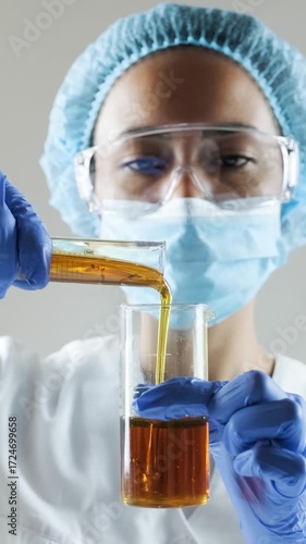 Scientist in lab coat and gloves examines golden oil in test tubes, pouring and analyzing samples.